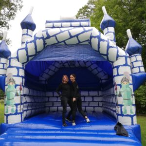 Eine blaue Ritter Hüpfburg mit zwei Teammitgliedern der Spassknöpfe