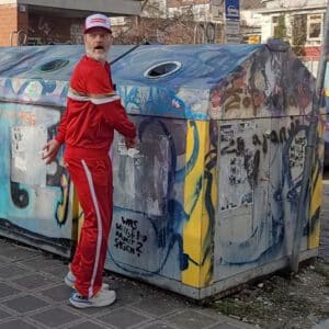 Guide blickt scherzhaft in bunten Streetart-Glascontainer während der Comedy Tour in Nürnberg.