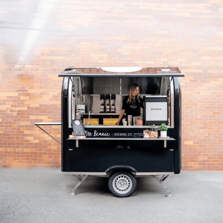 Junge Barista bei der Kaffeezubereitung am edlen schwarzen mobilen Kaffeewagen