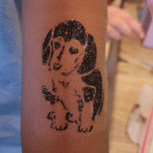 Glitzer-Tattoo eines schwarzen Hundemotivs auf dem Arm eines Kindes