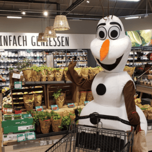 Ein symphatischer Schneemann-Maskottchen als Walking Act mit einem Einkaufswagen in Freising bei München in einem Rewe Supermarkt.