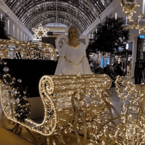 Ein festlicher Weihnachtsengel in einer prachtvoll beleuchteten Kutsche vor einer glitzernden Weihnachtskulisse im Einkaufscenter München Riem.