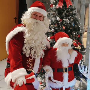 Ein großer und ein kleiner Weihnachtsmann geminsam vor einem schön geschmückten Weihnachtsbaum im Einkaufscenter München Riem.